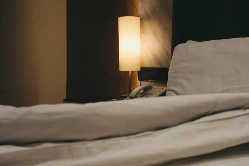 A bed with a white duvet and a bedside lamp glowing