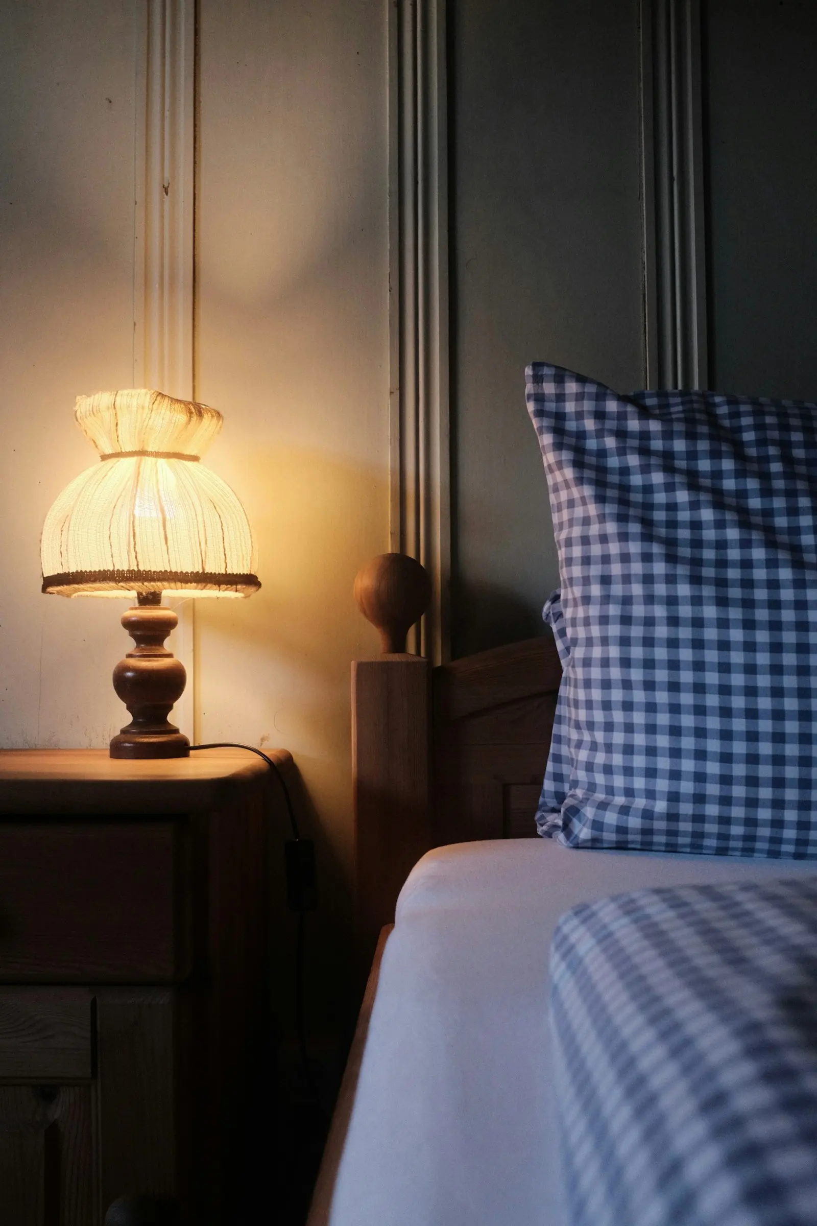 A bedside lamp glowing beside a bed with a checked pillow